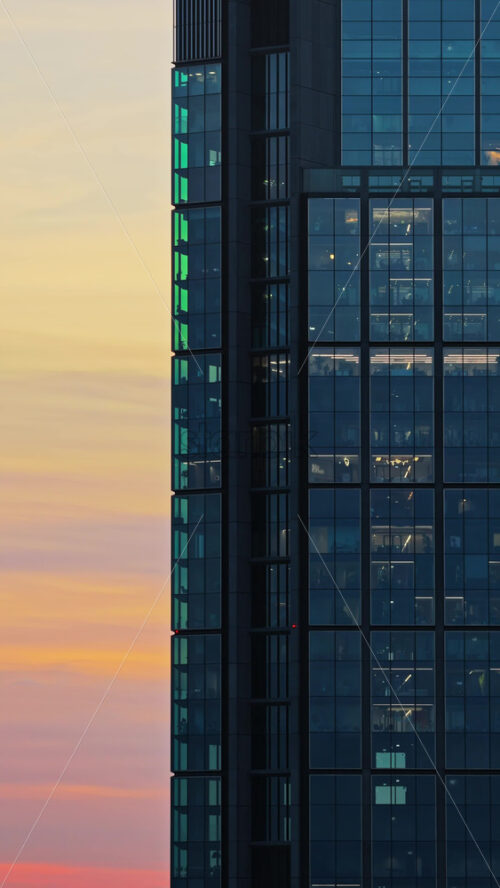 Video – Aerial drone view of the modern glass facade of the Warsaw Spire tower in the Wola district, capturing reflections of the city during sunset. Vertical - Starpik Stock