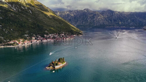 Video – Aerial drone view of the small natural island of Saint George, featuring a stone monastery surrounded by tall cypress trees on turquoise water. Bay of Kotor, Montenegro - Starpik Stock