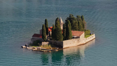 Video – Aerial drone view of the small natural island of Saint George, featuring a stone monastery surrounded by tall cypress trees on turquoise water. Bay of Kotor, Montenegro - Starpik Stock