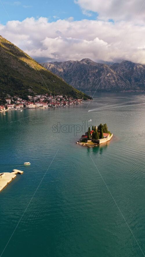 Video – Aerial drone view of the small natural island of Saint George, featuring a stone monastery surrounded by tall cypress trees on turquoise water. Bay of Kotor, Montenegro, Vertical - Starpik Stock