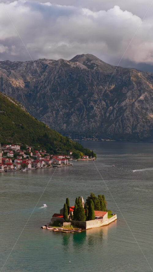 Video – Aerial drone view of the small natural island of Saint George, featuring a stone monastery surrounded by tall cypress trees on turquoise water. Vertical - Starpik Stock