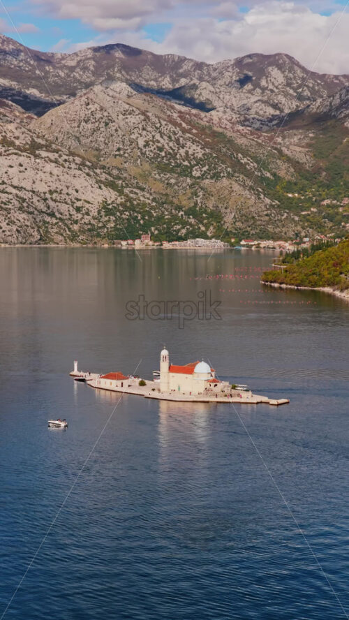 Video – Aerial drone view of the small natural island of Saint George, featuring a stone monastery surrounded by tall cypress trees on turquoise water. Vertical - Starpik Stock