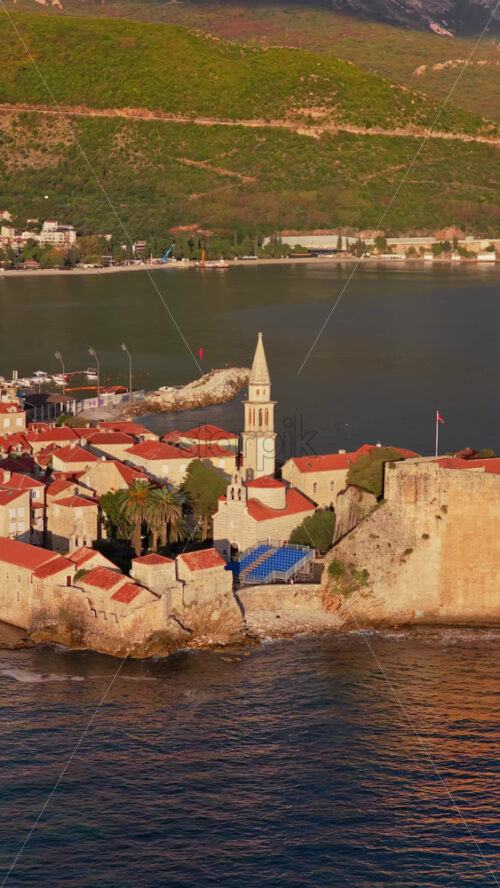 Video – Aerial drone view of the warm toned stone rooftops and narrow streets of Budva’s Old Town. Vertical - Starpik Stock
