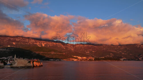 Video – Aerial drone view the mountains glow in orange light while the Budva Old Town sits along the water - Starpik Stock