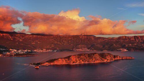 Video – Aerial drone view the mountains glow in orange light while the Budva Old Town sits along the water. Montenegro - Starpik Stock