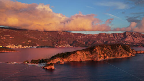 Video – Aerial drone view the mountains glow in orange light while the Budva Old Town sits along the water. Montenegro - Starpik Stock
