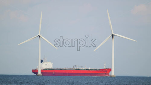 Video – Copenhagen, Denmark – August 4, 2025: Offshore wind turbines generating clean energy with a red cargo ship passing by on the ocean - Starpik Stock