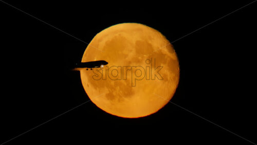 Video – Orange full moon illuminating the dark night sky with airplane passing. Slow motion - Starpik Stock