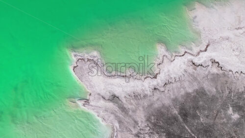 Video - Aerial drone view a mineral lake with bright turquoise water meeting textured white sediment
