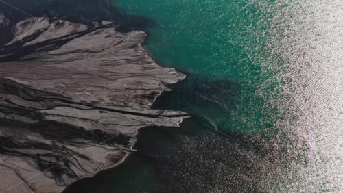 Video - Aerial drone view of turquoise waters meeting rugged, layered rock formations along the shoreline