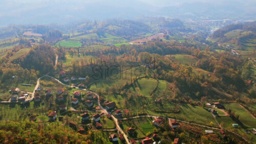 Video - Aerial drone view of a traditional Bosnian rural landscape with scattered homes, winding roads, farmland, and forested hills