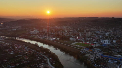 Video - Aerial drone view of an urban cityscape with the sun setting behind distant hills in Bosnia and Herzegovina