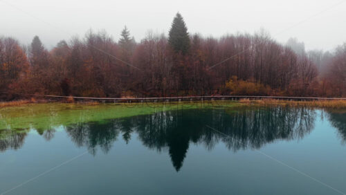Video - Aerial drone view of a calm lake surrounded by dense autumn forest under a layer of morning fog in Plitvice Lakes National Park, Croatia