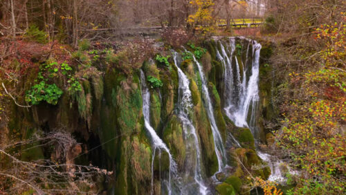 Video - Aerial drone view of cascading waterfalls flowing over moss covered cliffs and lush vegetation in Plitvice Lakes National Park, Croatia