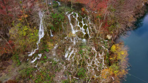 Video - Aerial drone view of cascading waterfalls flowing over moss covered cliffs and lush vegetation in Plitvice Lakes National Park, Croatia