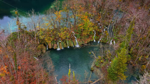 Video - Aerial drone view hidden waterfalls flowing into emerald lakes, surrounded by thick forest and rugged limestone formations. Plitvice Lakes National Park, Croatia