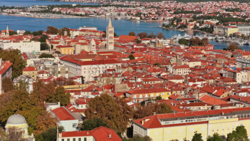 Video - Aerial drone view over Zadar's historic Old Town showcasing a dense pattern of terracotta rooftops, Romanesque churches, medieval towers, and narrow streets