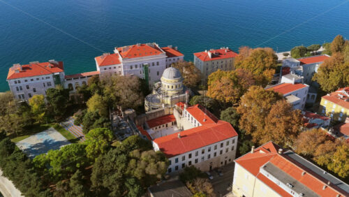 Video - Aerial drone view of the University of Zadar campus and the historic Scientific Library dome surrounded by red roofed buildings and lush autumn trees