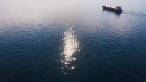 Video - Aerial drone view of an oil tanker traveling across open Adriatic waters with distant mountain ridges and coastal towns visible on the horizon. Water sparkling reflection
