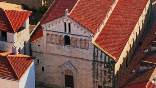 Video - Aerial drone view of an old stone church facade with arched windows, decorative stonework, and weathered textures. Zadar, Croatia