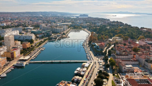 Video - Aerial drone view of the waterway splitting the city, with bridges, marinas, and modern and historic buildings stretching into the distance. Zadar Croatia