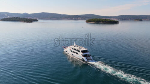 Video - Aerial drone view of a white passenger yacht cruising through smooth blue water, framed by forested islands and hills. Biograd na Moru, Croatia