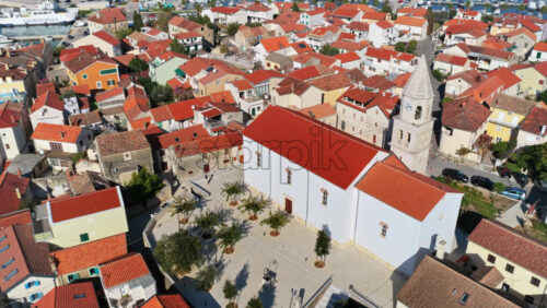 Video - Aerial drone view of Biograd's compact Old Town, centered around the white church of St. Anastasia with its tall stone bell tower. Biograd na Moru, Croatia
