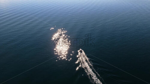 Video - Aerial drone view of a small motorboat speeding across the water, leaving a white foamy trail behind it on the calm turquoise sea