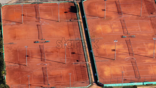 Video - Aerial drone view of multiple clay tennis courts arranged side by side, with visible nets, lines, and shadows