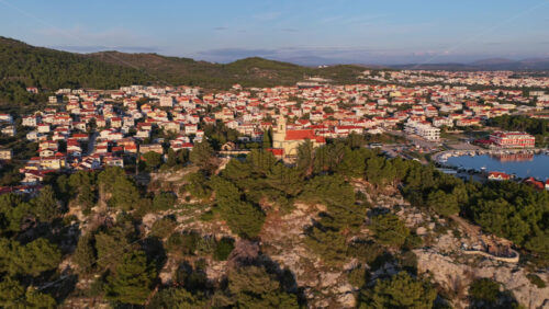 Video - Aerial drone view of a small stone church with a bell tower at golden hour sunset in Tribunj, Croatia