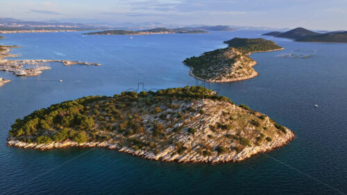 Video - Aerial drone view of several rocky, pine covered islands stretching across the calm blue waters of Croatia near Tribunj