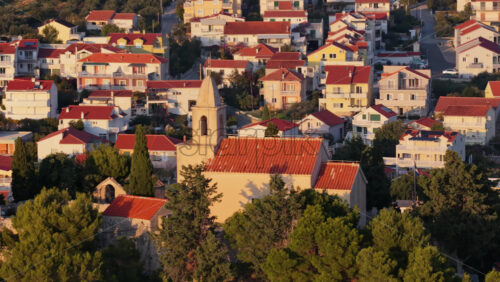Video - Aerial drone view of a small stone church with a bell tower at golden hour sunset in Tribunj, Croatia