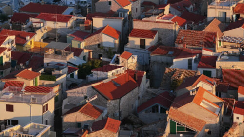 Video - Aerial drone view of Tribunj residential area near the marina, showing clusters of red roofed homes with the harbor and anchored boats visible in the background. Croatia