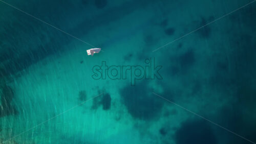 Video - Aerial drone view of a white sailboat gliding smoothly over calm turquoise water