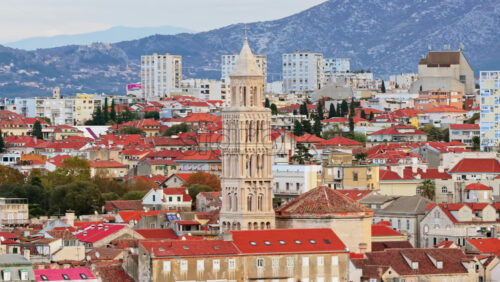 Video - Aerial drone view of the iconic bell tower of Split rising above red rooftops with mountains in the background
