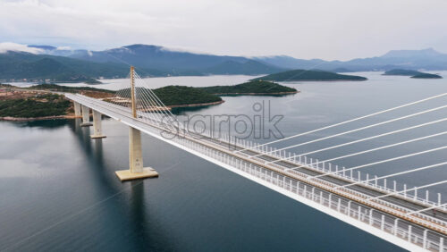 Video - Aerial drone view of the Peljesac Bridge near Komarna, Croatia, partially shrouded in low coastal fog with mountains in the background