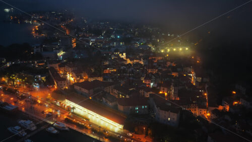 Video - Aerial drone view of orange streetlights illuminate the tightly packed buildings, while mist rolls in from the hills in the Bay of Kotor