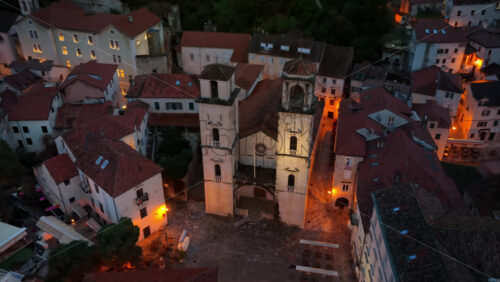 Video - Aerial drone view of the Cathedral of Saint Tryphon surrounded by medieval stone buildings at dusk, showing the historic architecture in warm lighting. Kotor, Montenegro