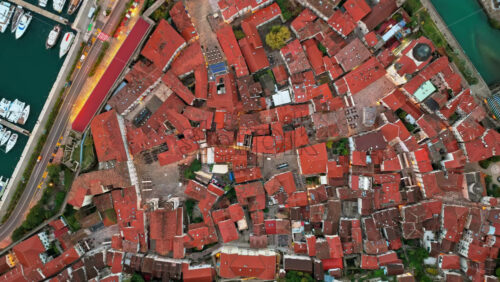 Video - Aerial drone view of the medieval street maze of Kotor's Old Town, showing red rooftops, narrow alleys, and the marina along the bay