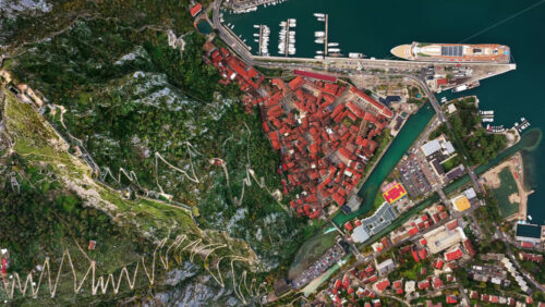 Video - Aerial drone view of the famous zig zag hiking path leading to the fortress, next to the red roofs of Kotor Old Town and the marina