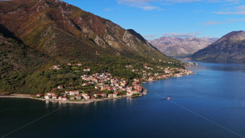 Video - Aerial drone view of a seaside neighborhood with red rooftops, tree lined streets, and small piers along the shoreline. Bay of Kotor, Montenegro
