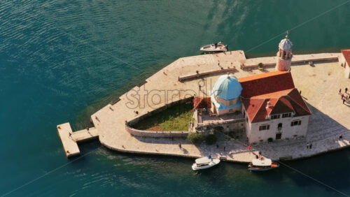 Video - Aerial drone view of Saint George Island near Perast, featuring its stone monastery, cypress trees, and surrounding turquoise water. Bay of Kotor, Montenegro