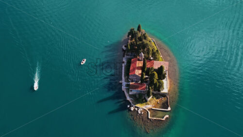 Video - Aerial drone view of the small natural island of Saint George, featuring a stone monastery surrounded by tall cypress trees on turquoise water. Bay of Kotor, Montenegro