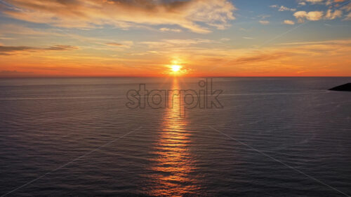 Video - Aerial drone view of a sunset across the open Adriatic Sea, with the sun descending and reflecting golden light on the waves. Montenegro