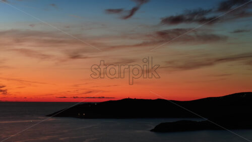 Video - Aerial drone view of a vivid sunset over calm open sea, with warm orange and red tones glowing across the horizon. Montenegro