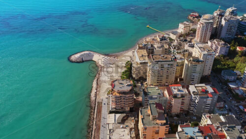 Video - Aerial drone view of the Durres coastline showing tall apartment buildings, turquoise sea, and the uniquely shaped waterfront platform extending into the water