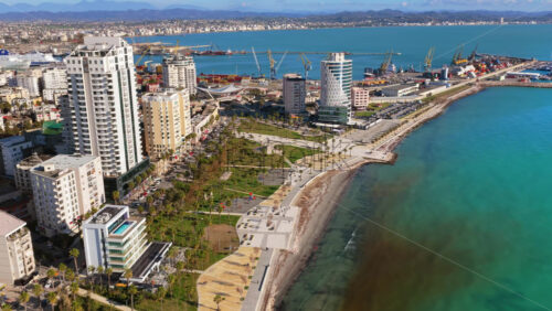 Video - Aerial drone view of the green waterfront park, tall residential towers, sports courts, and the large industrial port in the distance in Durres, Albania