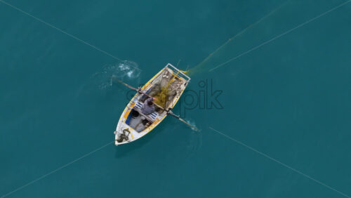 Video - Aerial drone view of a fisherman rowing through deep turquoise waters along the Vlora coastline, with nets and equipment visible on the rustic boat