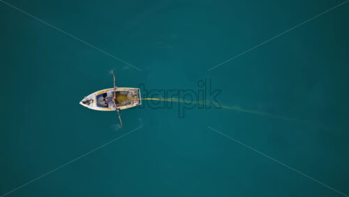 Video - Aerial drone view of a fisherman rowing through deep turquoise waters along the Vlora coastline, with nets and equipment visible on the rustic boat