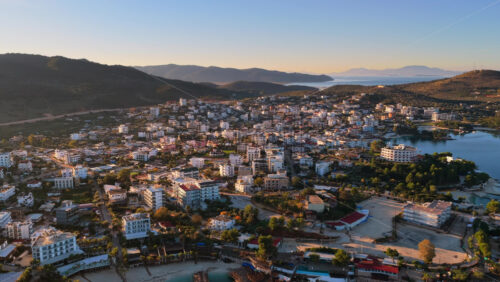 Video - Aerial drone view of Ksamil town, its dense cluster of hotels and houses, and the iconic bright blue bays with floating platforms and beach clubs